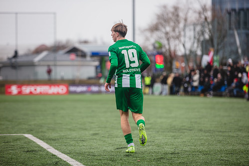 A soccer player wearing a green jersey with white stripes and the number 19 on the back, running on a grass field during a match.